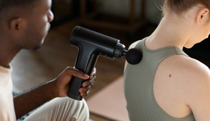 Un homme qui utilise un pistolet de massage pour masser le dos d'une femme