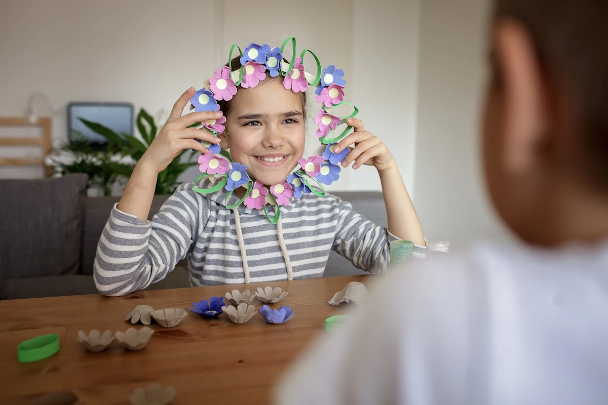 Une petite fille qui montre un collier de fleurs en carton colorés