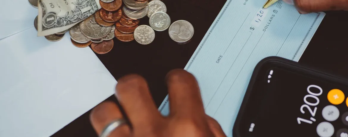 Une personne qui écrit un chèque près de plusieurs pièces de monnaies et d'une calculatrice