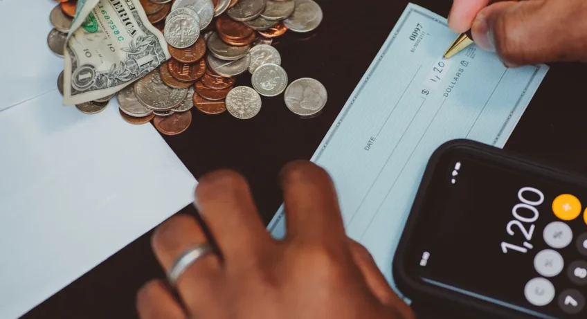 Une personne qui écrit un chèque près de plusieurs pièces de monnaies et d'une calculatrice