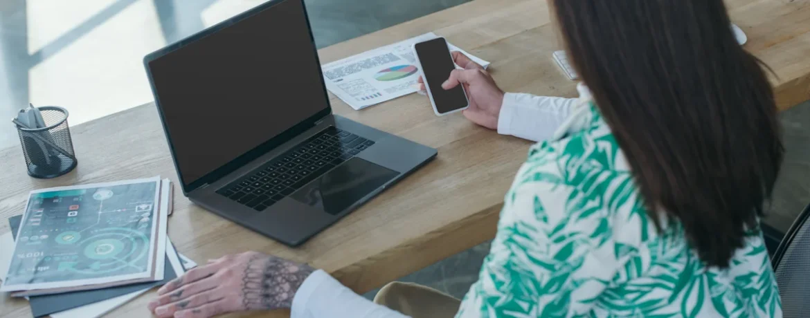 Une femme qui est sur son ordinateur et qui regarde son smartphone en même temps